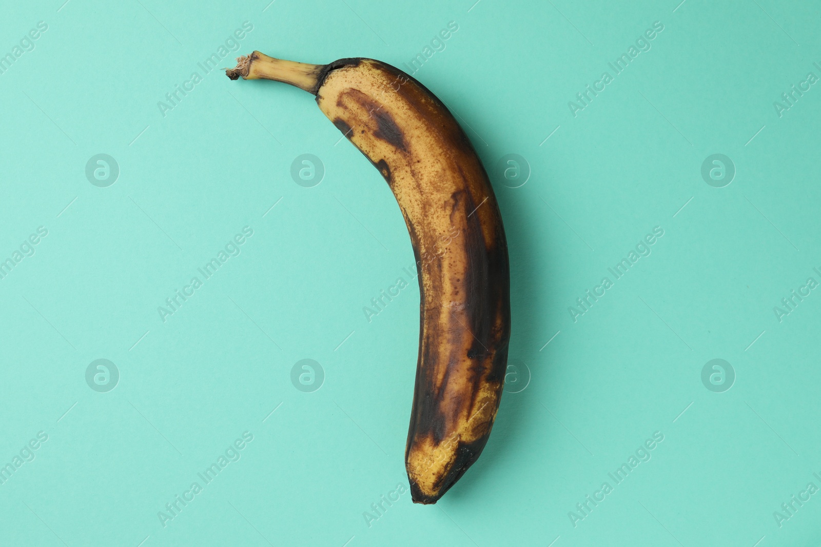 Photo of Overripe banana with dark spots on turquoise background, top view