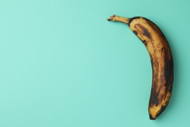 Photo of Overripe banana with dark spots on turquoise background, top view. Space for text