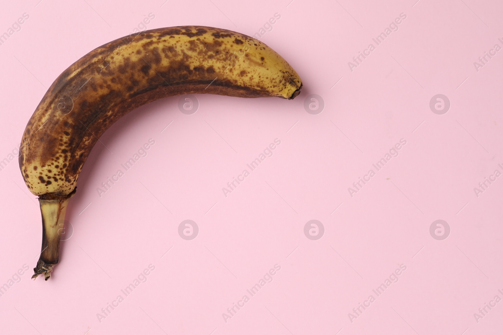 Photo of Overripe banana with dark spots on pink background, top view. Space for text