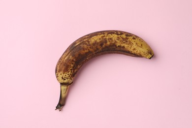 Photo of Overripe banana with dark spots on pink background, top view