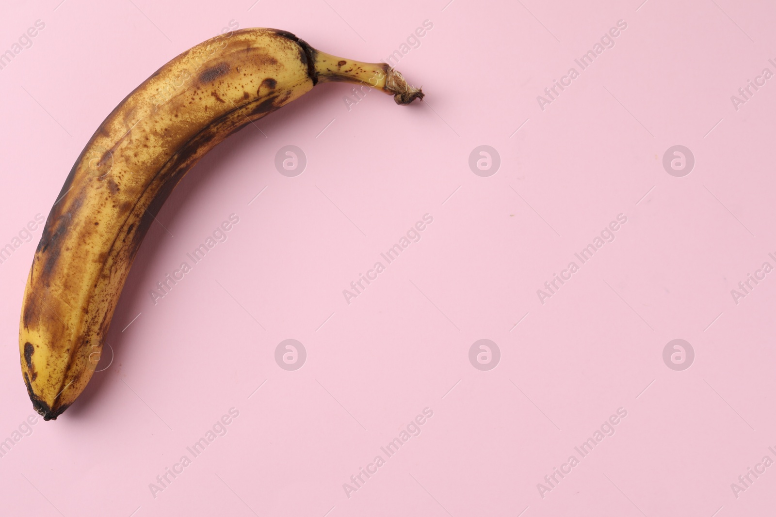 Photo of Overripe banana with dark spots on pink background, top view. Space for text