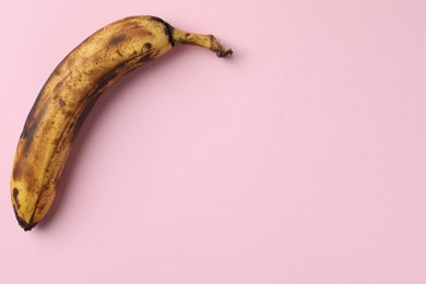 Overripe banana with dark spots on pink background, top view. Space for text