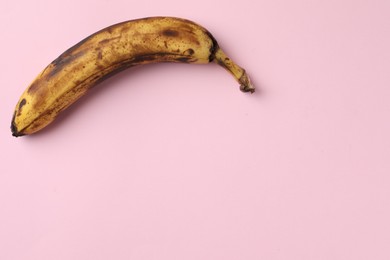 Overripe banana with dark spots on pink background, top view. Space for text