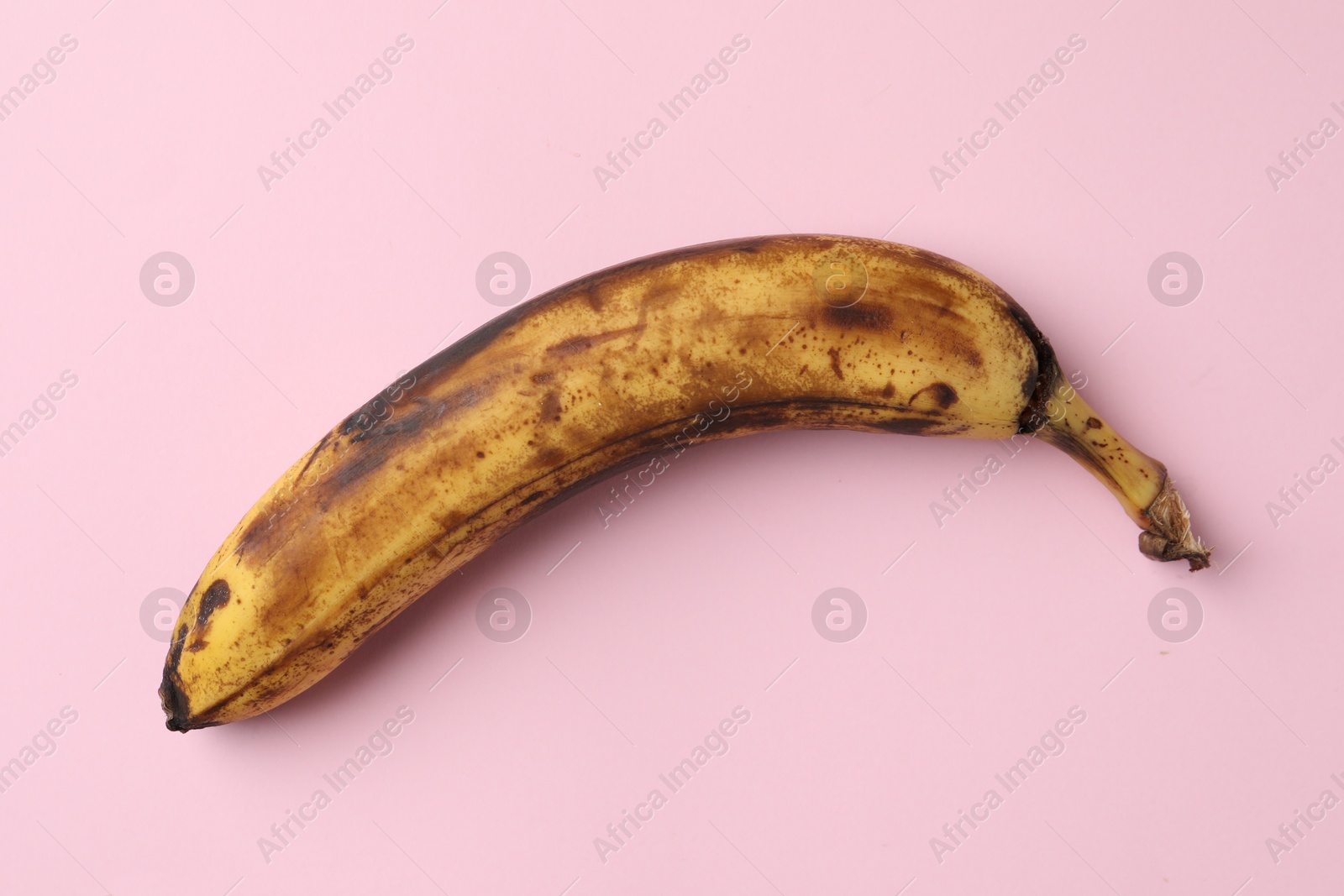 Photo of Overripe banana with dark spots on pink background, top view