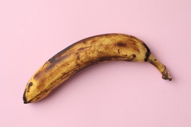 Photo of Overripe banana with dark spots on pink background, top view