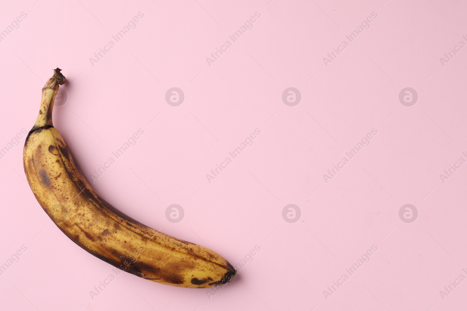 Photo of Overripe banana with dark spots on pink background, top view. Space for text