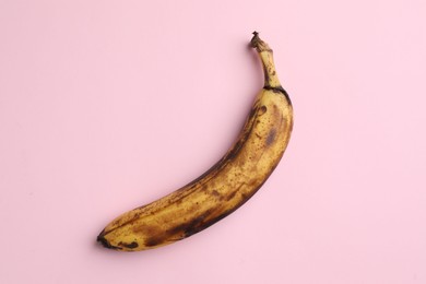 Overripe banana with dark spots on pink background, top view