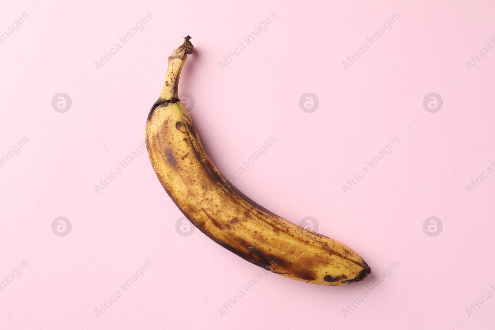 Photo of Overripe banana with dark spots on pink background, top view