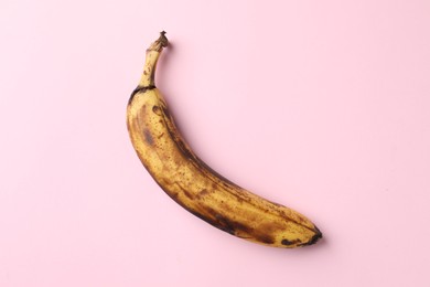 Photo of Overripe banana with dark spots on pink background, top view