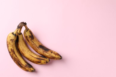 Bunch of ripe bananas with dark spots on pink background, top view. Space for text