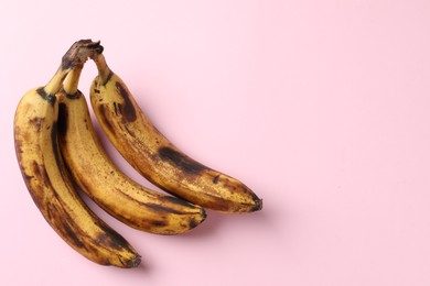 Bunch of ripe bananas with dark spots on pink background, top view. Space for text