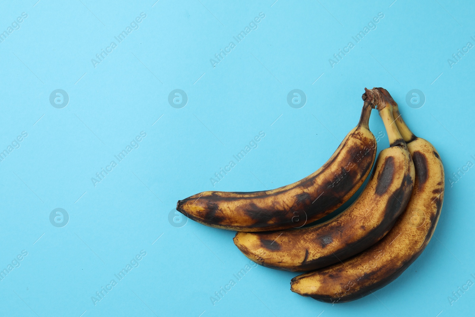 Photo of Bunch of ripe bananas with dark spots on light blue background, top view. Space for text