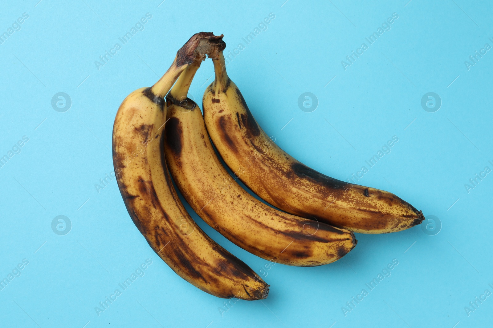 Photo of Bunch of ripe bananas with dark spots on light blue background, top view