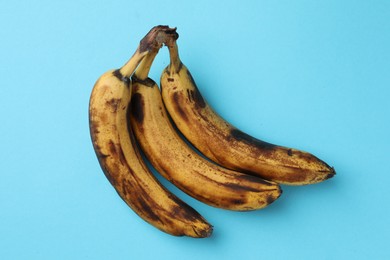 Bunch of ripe bananas with dark spots on light blue background, top view