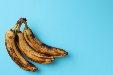 Bunch of ripe bananas with dark spots on light blue background, top view. Space for text