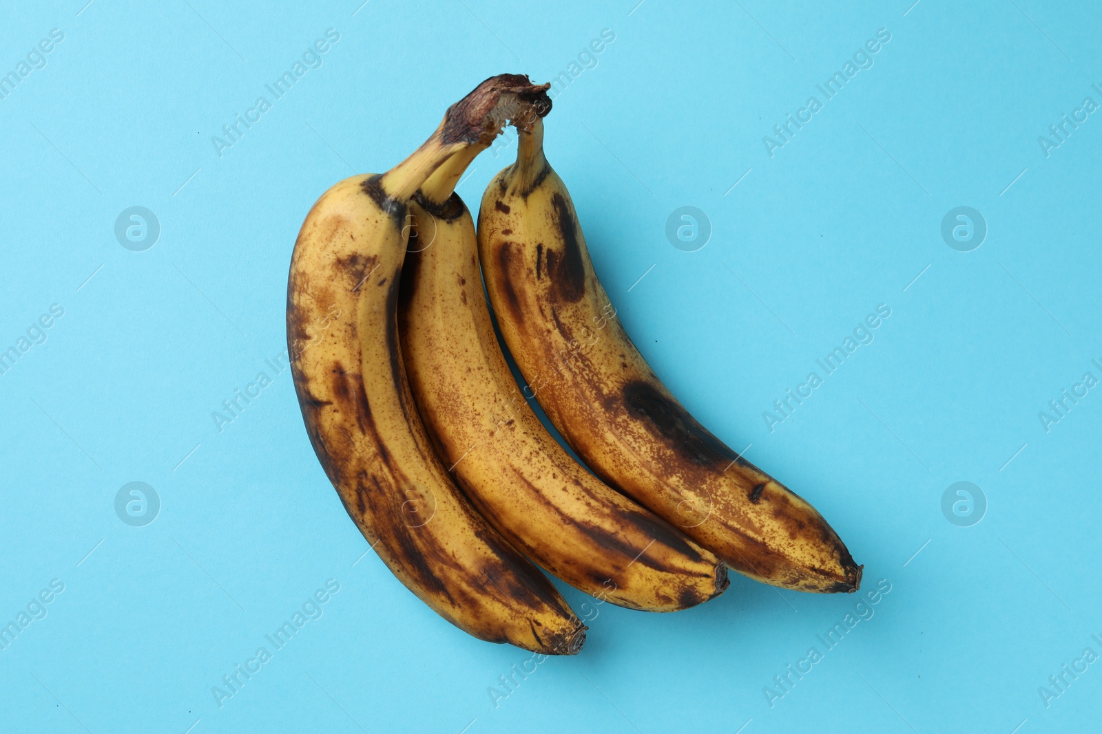 Photo of Bunch of ripe bananas with dark spots on light blue background, top view