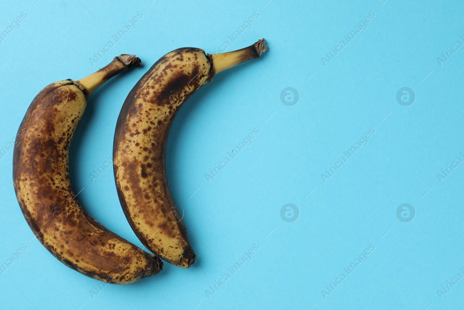 Photo of Overripe bananas with dark spots on light blue background, top view. Space for text