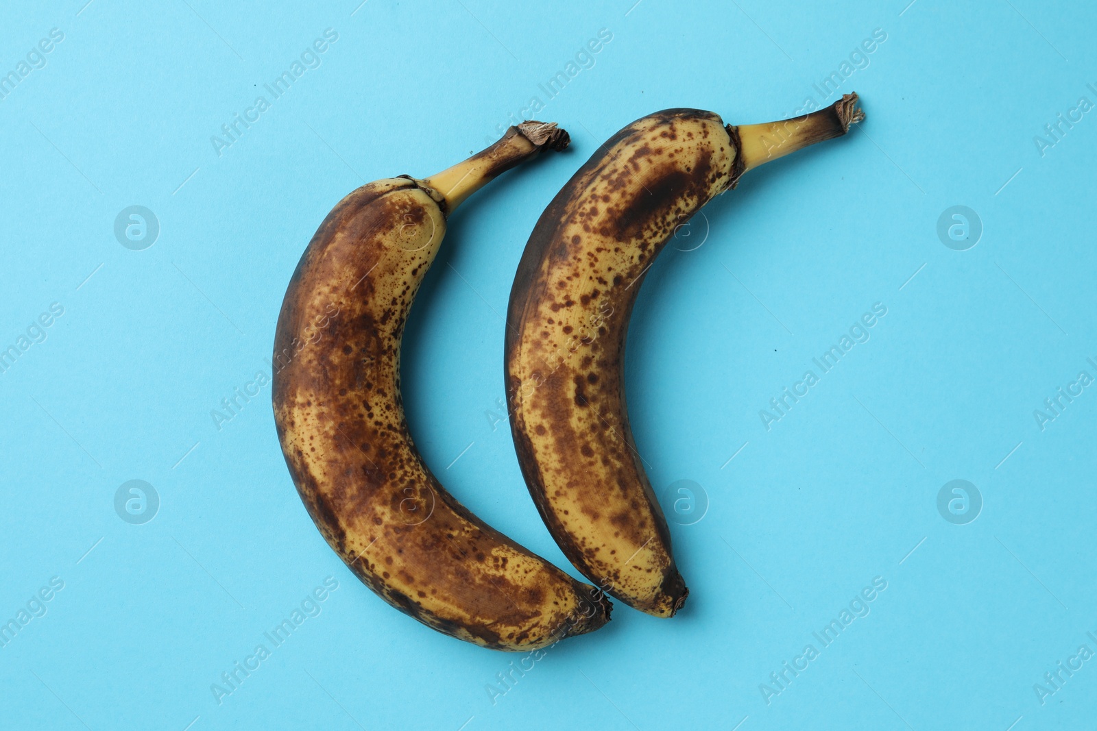 Photo of Overripe bananas with dark spots on light blue background, top view