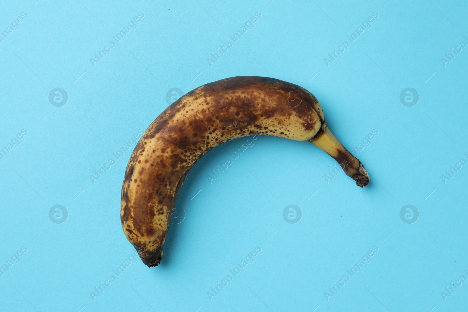 Photo of Overripe banana with dark spots on light blue background, top view