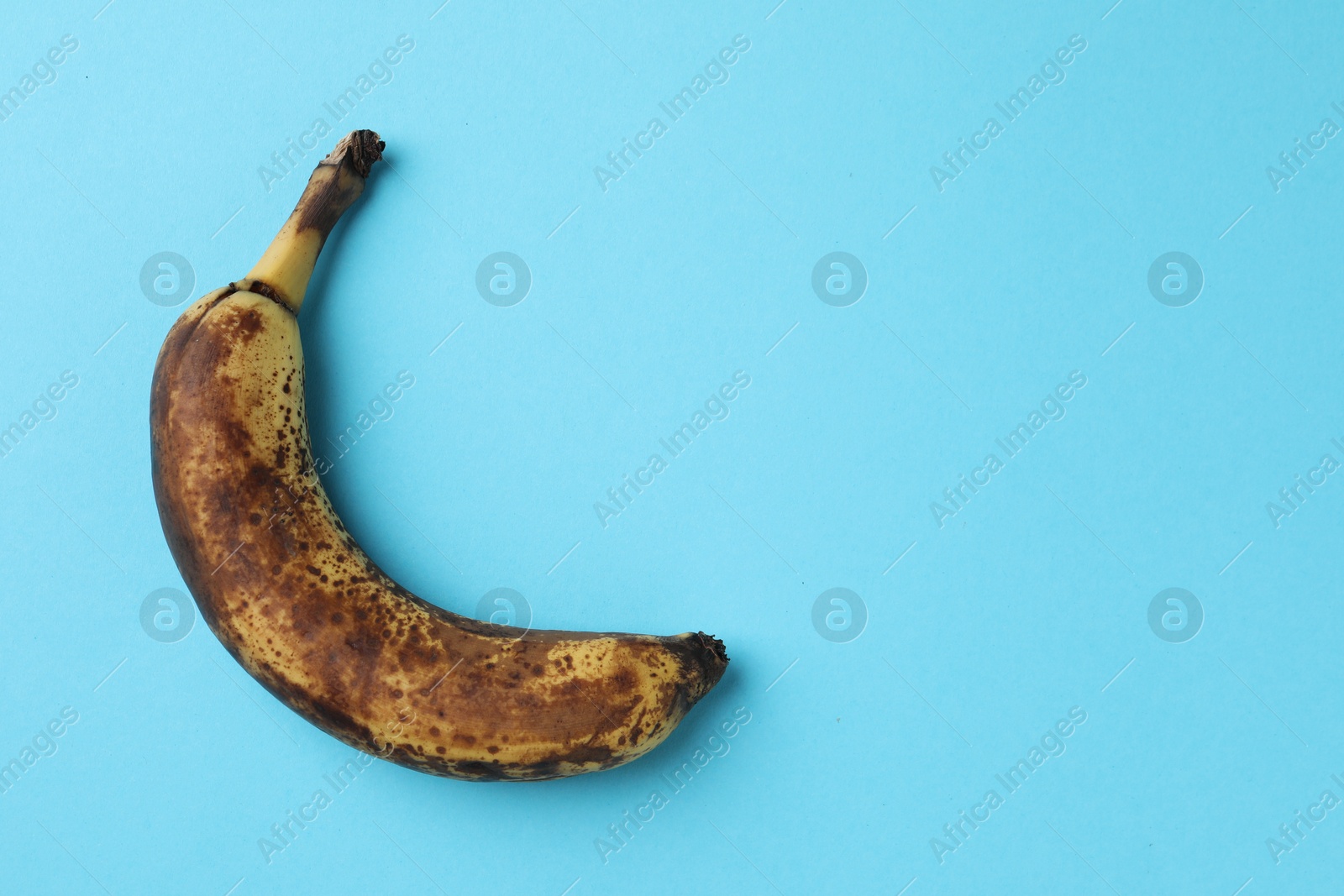 Photo of Overripe banana with dark spots on light blue background, top view. Space for text