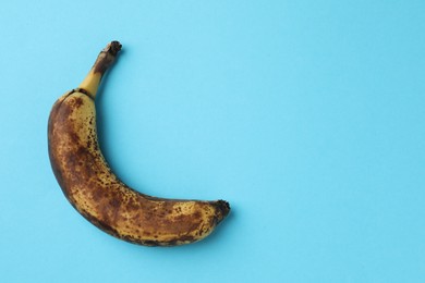 Overripe banana with dark spots on light blue background, top view. Space for text