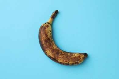 Overripe banana with dark spots on light blue background, top view