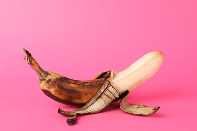 Overripe banana with dark spots on pink background