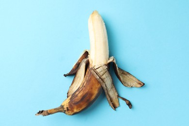 Overripe banana with dark spots on light blue background, top view