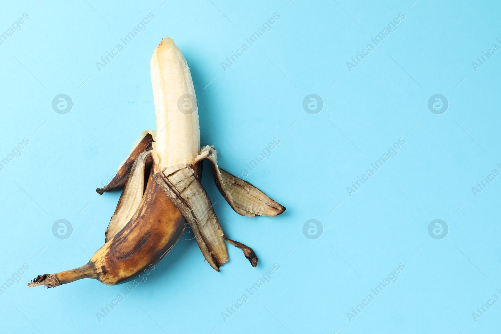 Photo of Overripe banana with dark spots on light blue background, top view. Space for text