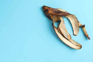 Photo of Banana peel with dark spots on light blue background, top view. Space for text