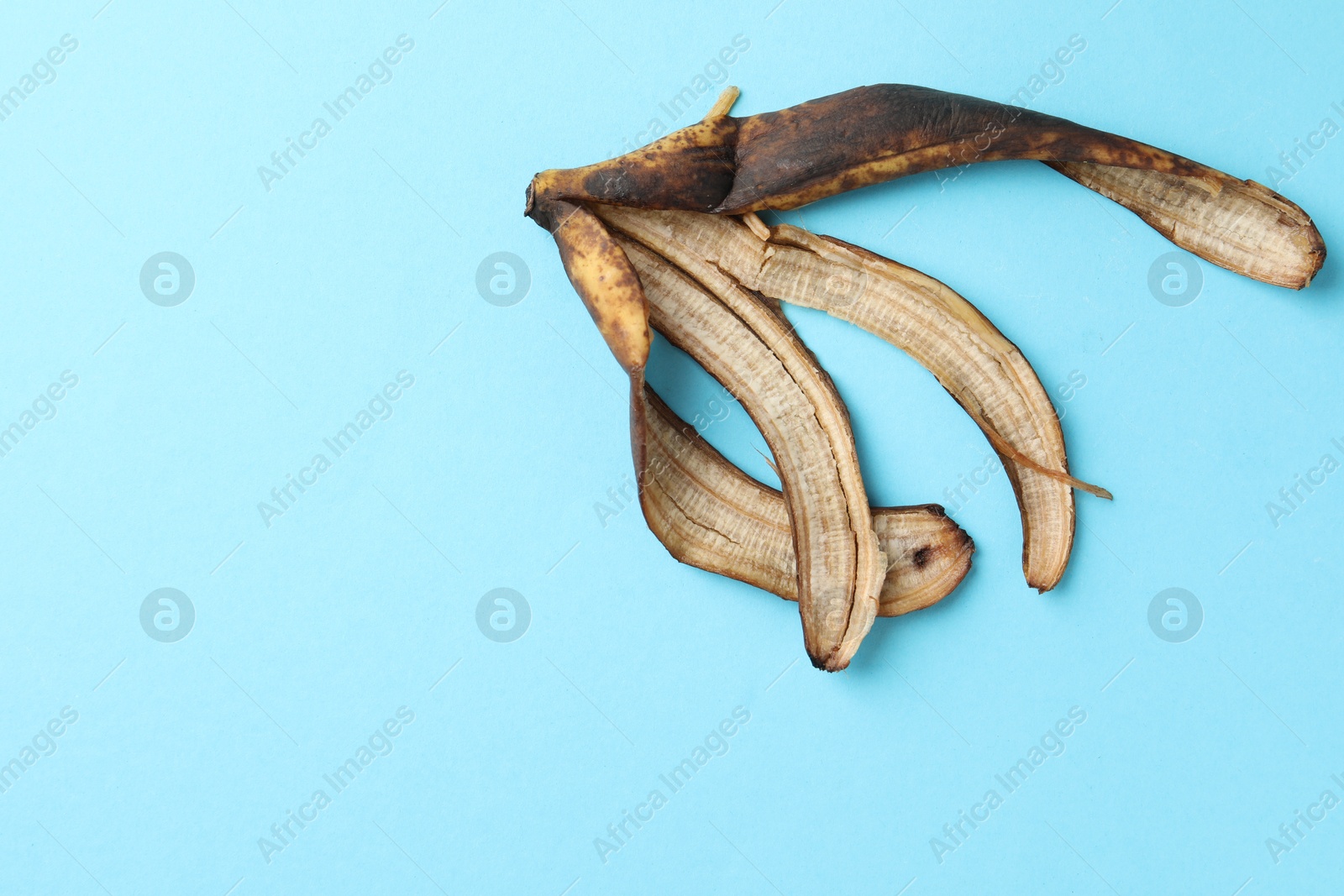 Photo of Banana peel with dark spots on light blue background, top view. Space for text