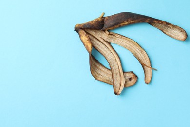 Banana peel with dark spots on light blue background, top view. Space for text