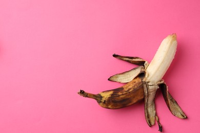 Overripe banana with dark spots on pink background, top view. Space for text