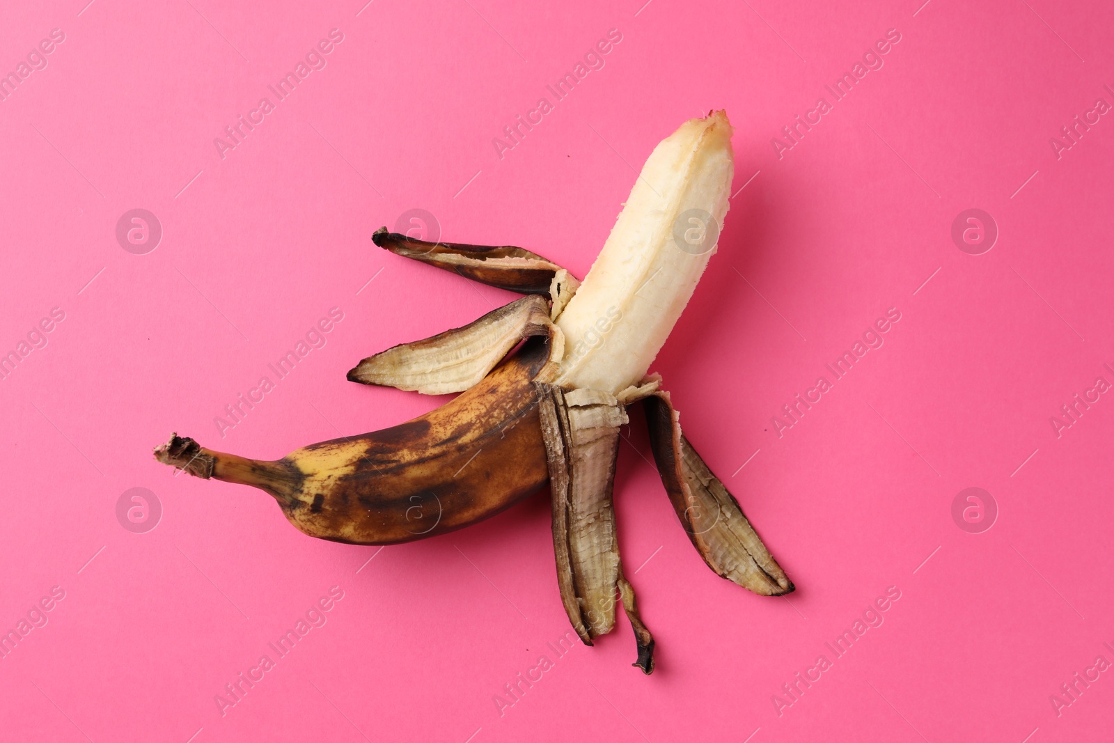 Photo of Overripe banana with dark spots on pink background, top view