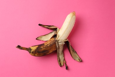 Overripe banana with dark spots on pink background, top view