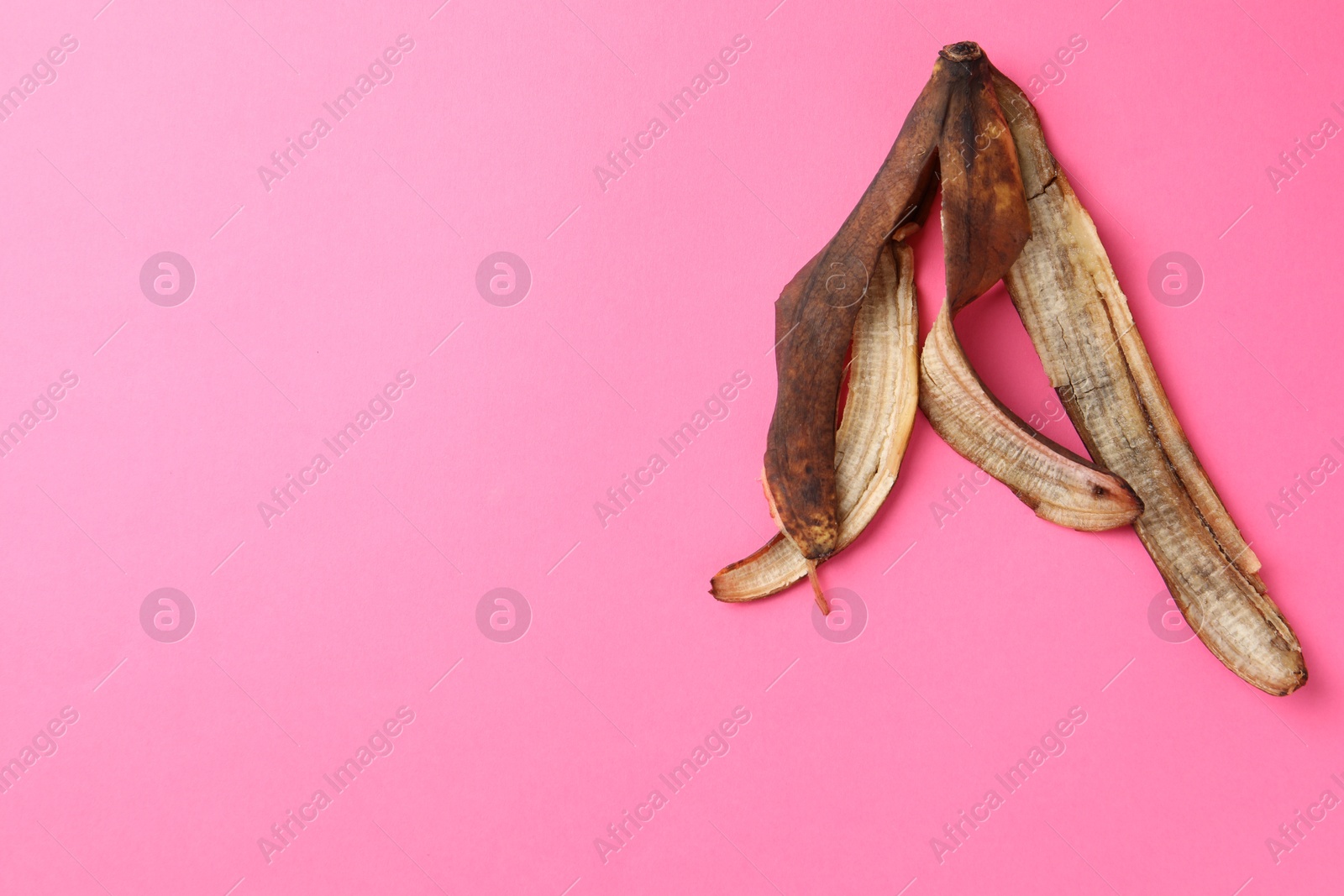 Photo of Banana peel with dark spots on pink background, top view. Space for text