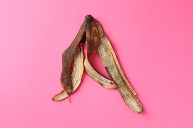 Banana peel with dark spots on pink background, top view