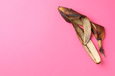 Banana peel with dark spots on pink background, top view. Space for text