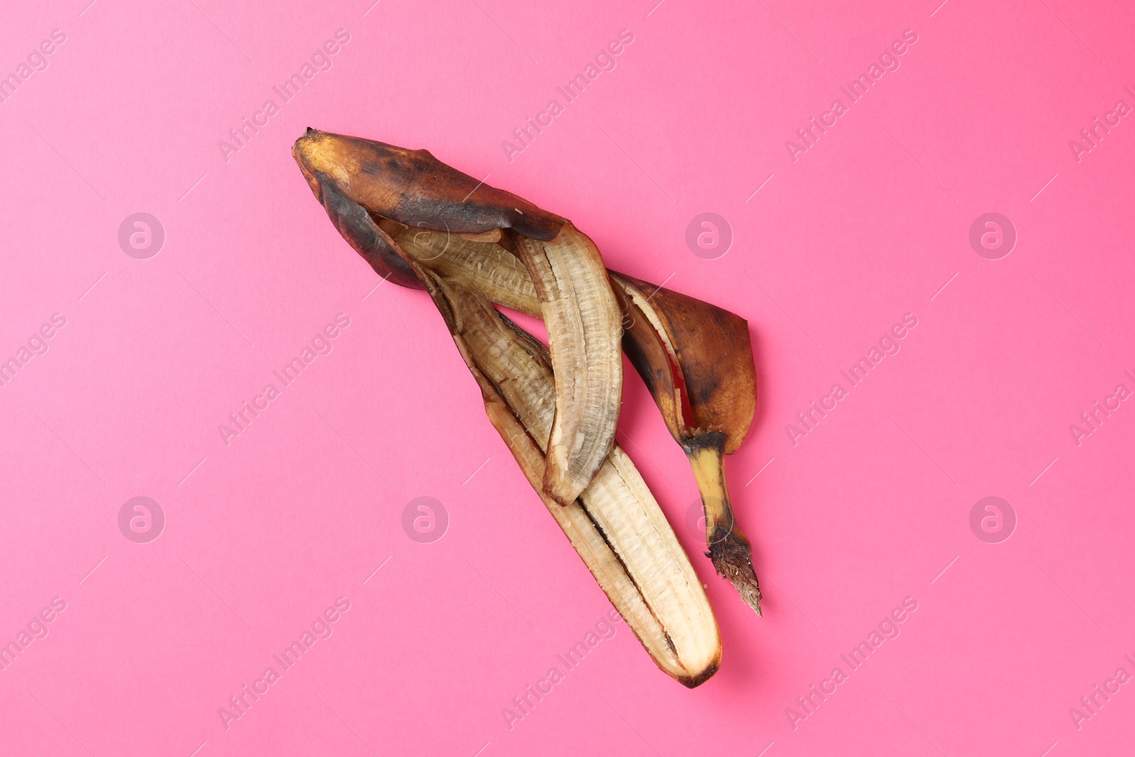 Photo of Banana peel with dark spots on pink background, top view