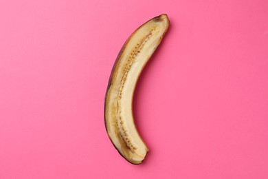 Half of overripe banana on pink background, top view