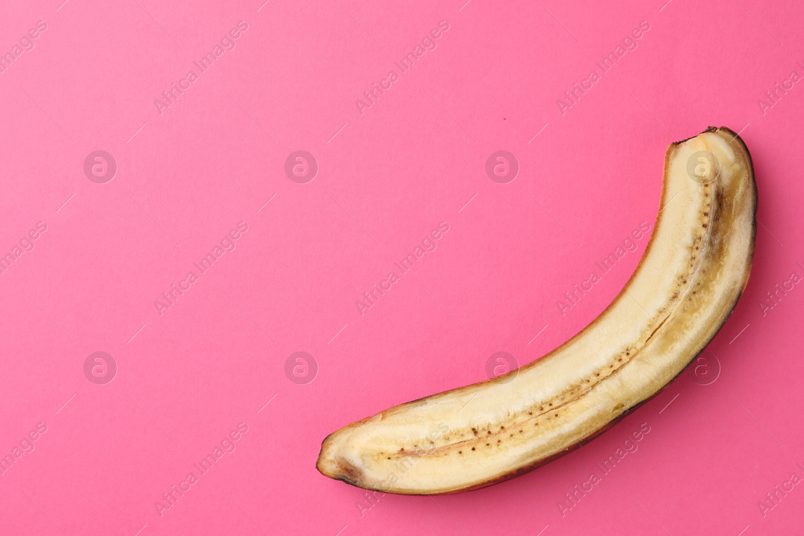 Photo of Half of overripe banana on pink background, top view. Space for text