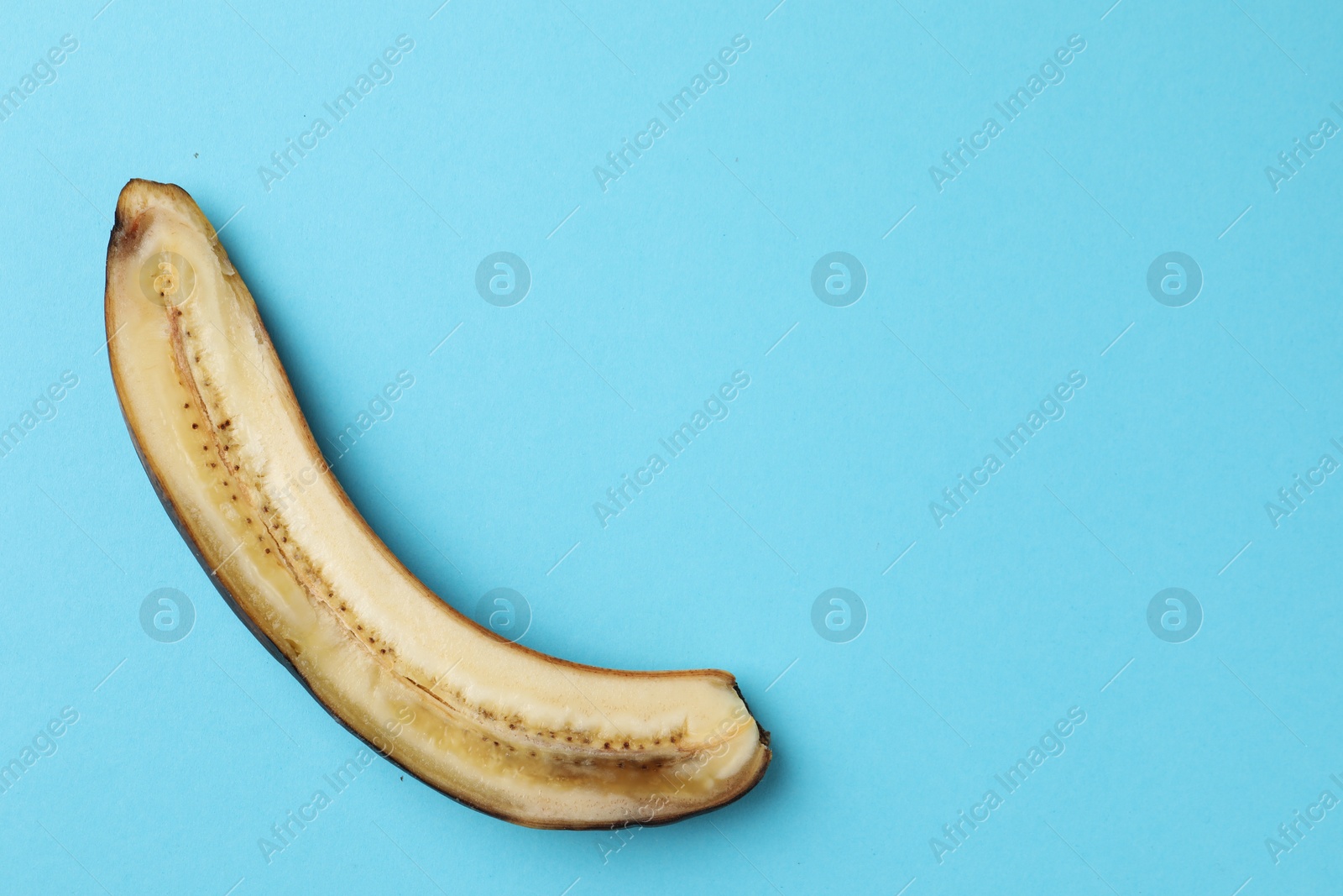 Photo of Half of overripe banana on light blue background, top view. Space for text