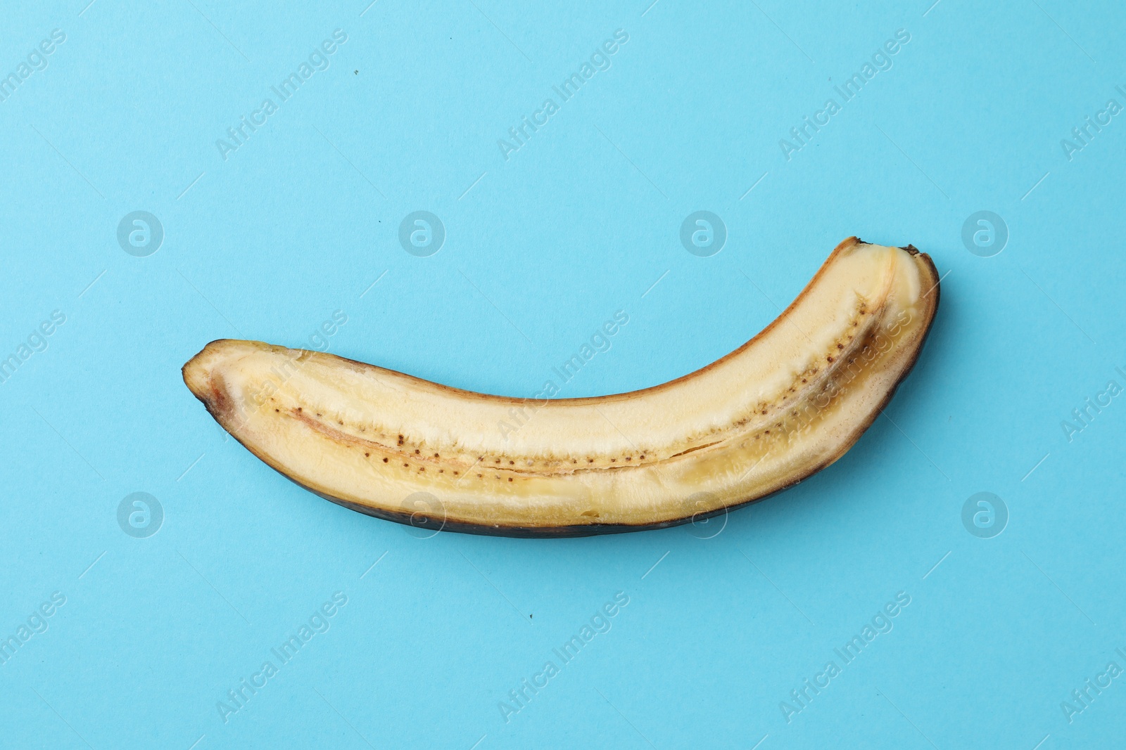 Photo of Half of overripe banana on light blue background, top view