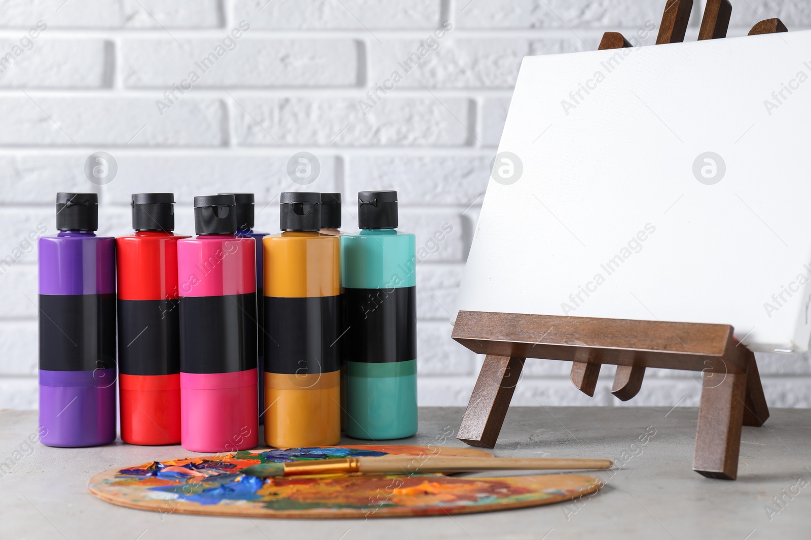 Photo of Acrylic paints of different colors in bottles, palette, brushes and blank canvas on light grey table