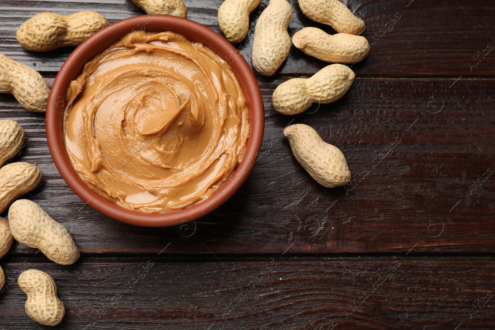 Photo of Tasty peanut butter in bowl and nuts on wooden table, flat lay. Space for text