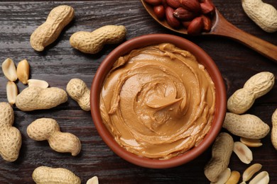 Photo of Tasty peanut butter in bowl and nuts on wooden table, flat lay