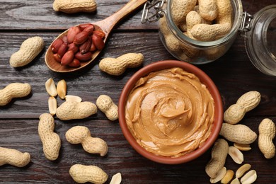 Photo of Tasty peanut butter in bowl, nuts, jar and spoon on wooden table, flat lay