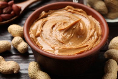 Photo of Tasty peanut butter in bowl and groundnuts on table, closeup