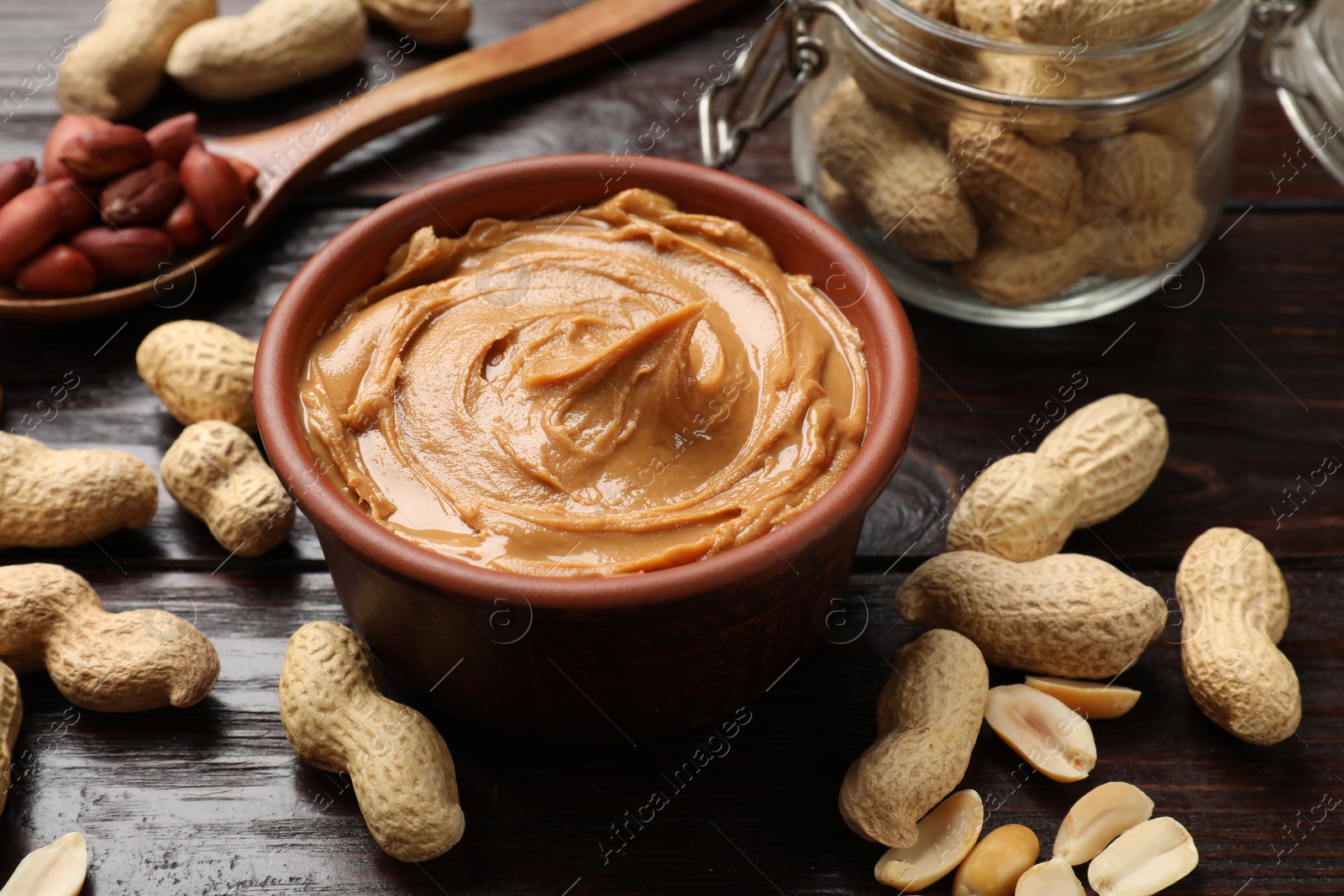 Photo of Tasty peanut butter in bowl, groundnuts, jar and spoon on wooden table, closeup