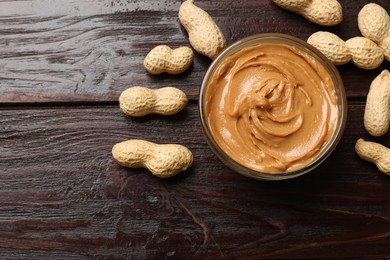 Photo of Tasty peanut butter in bowl and nuts on wooden table, flat lay. Space for text